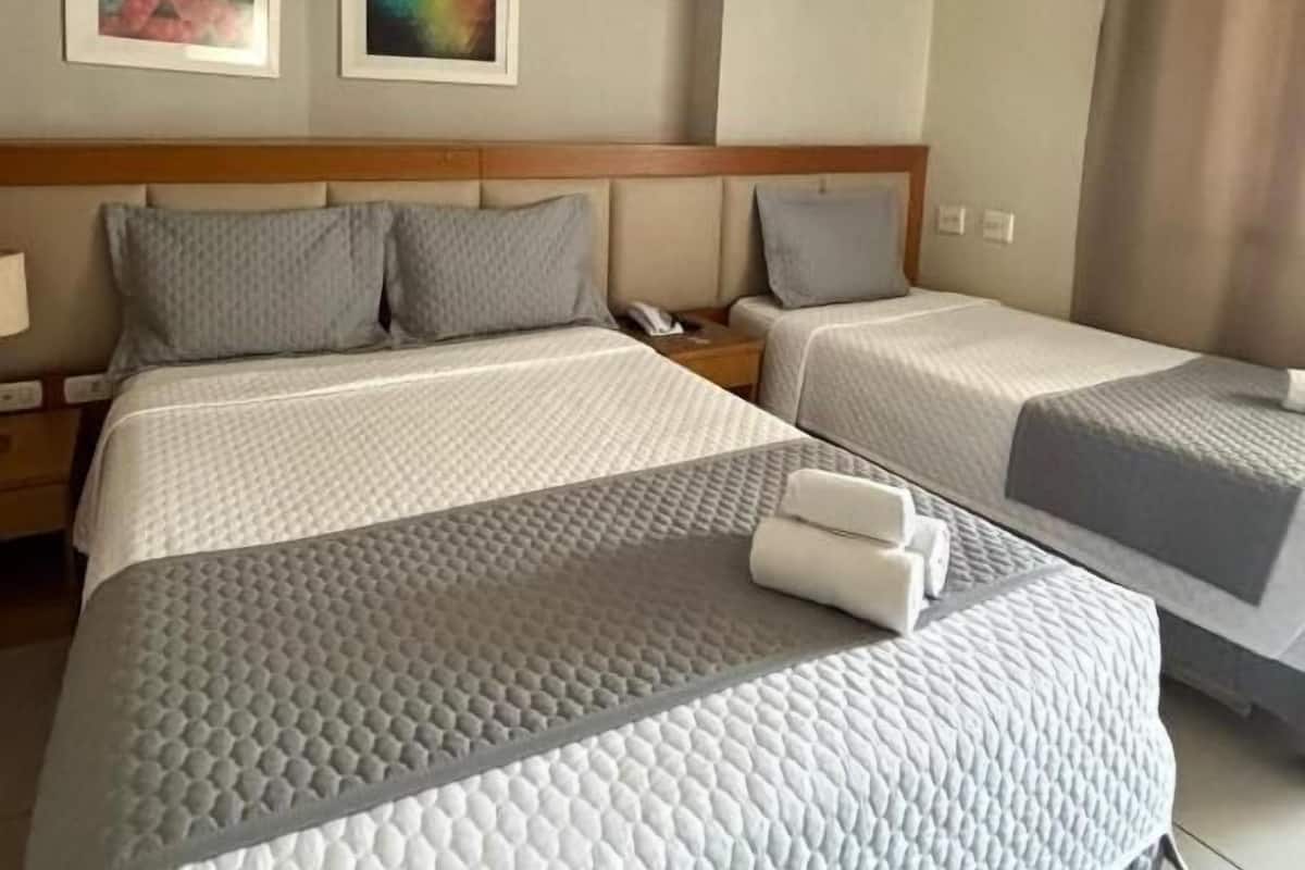 A hotel room with two beds, a wooden headboard, a nightstand with a phone, and two framed artworks on the wall.