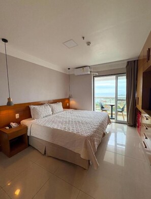 Una habitación de hotel con una cama grande, una mesita de noche, un equipo de aire acondicionado, un televisor y un balcón con vistas.