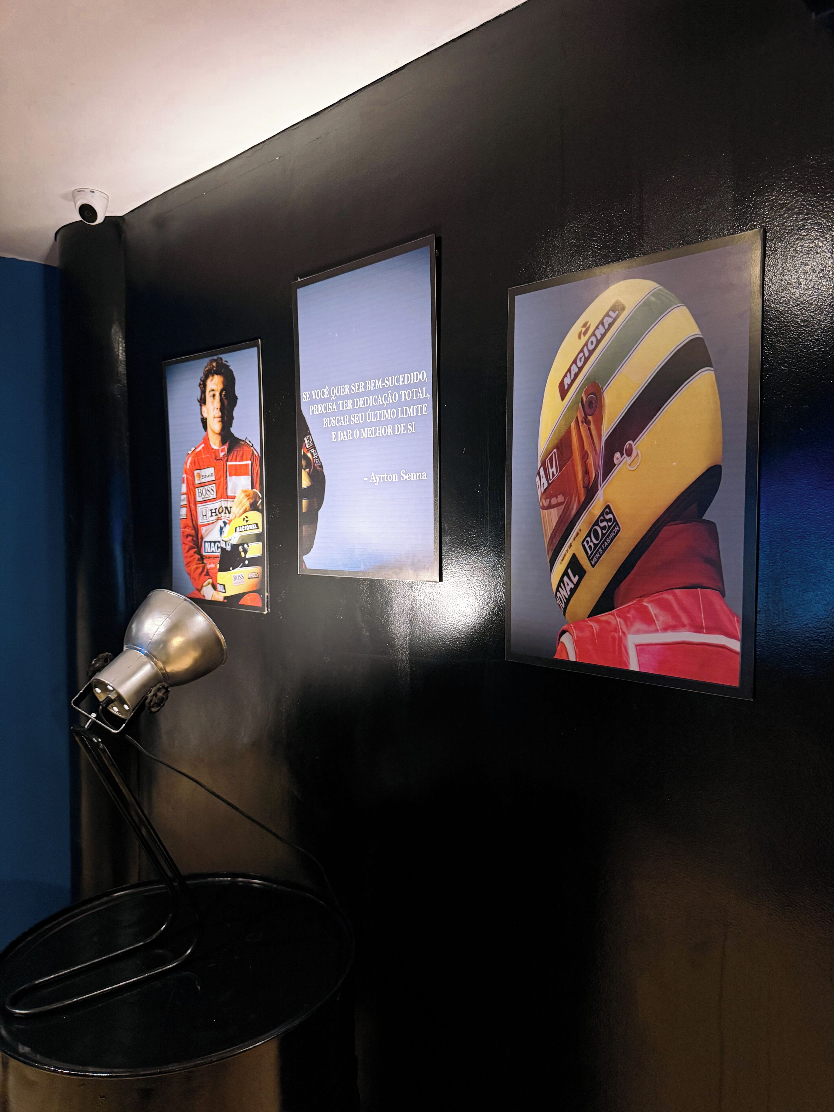 Pared con tres elementos enmarcados: un póster de un piloto de carreras, una cita motivacional y un casco.