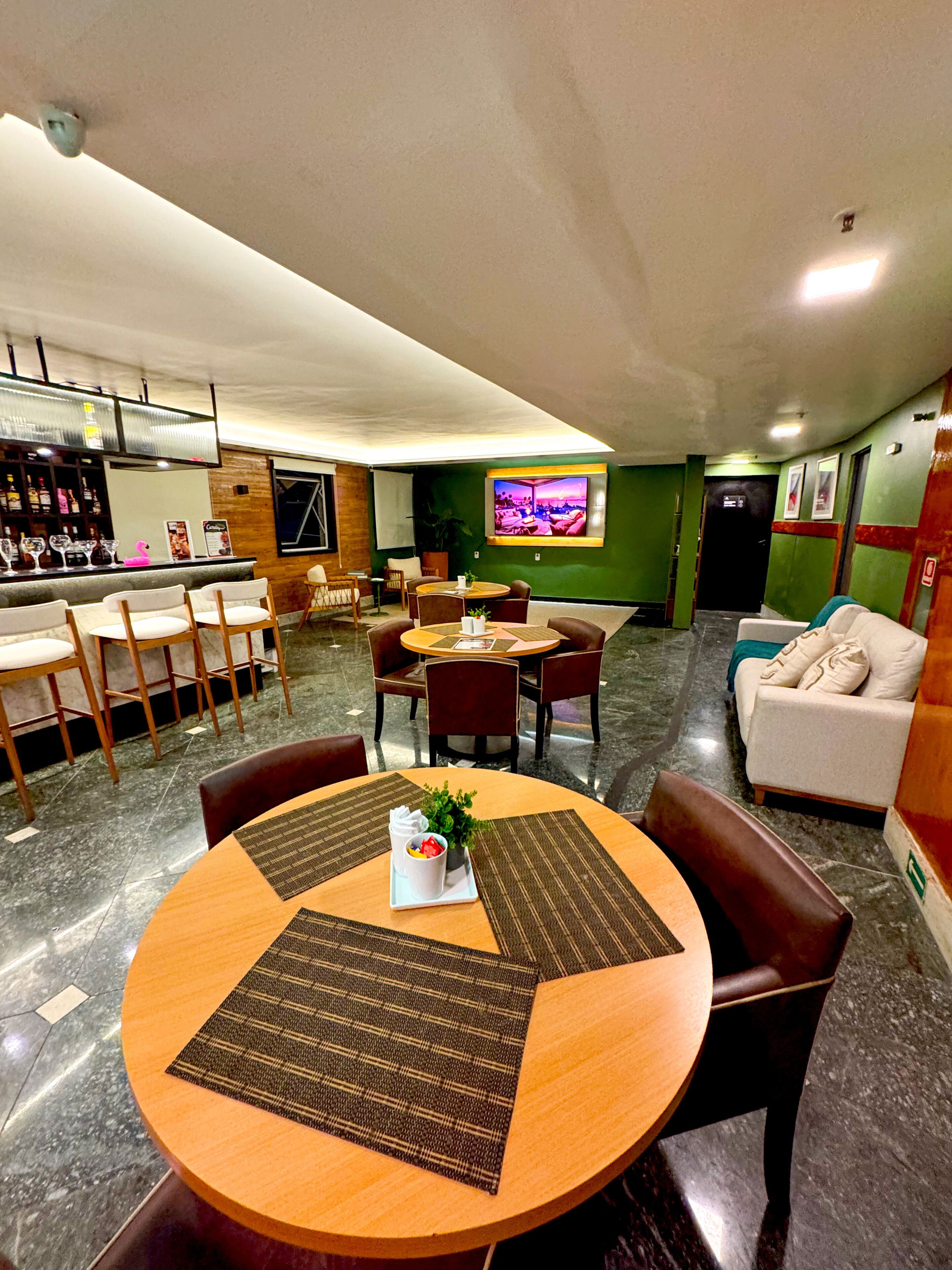 A hotel lobby with a bar area, seating arrangements, and a television screen.