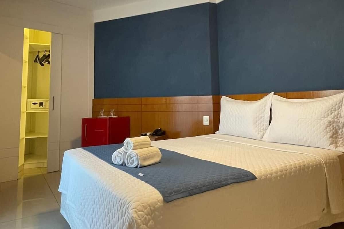 A hotel room with a large bed, a wooden headboard, a bedside table with a lamp, and a red cabinet.