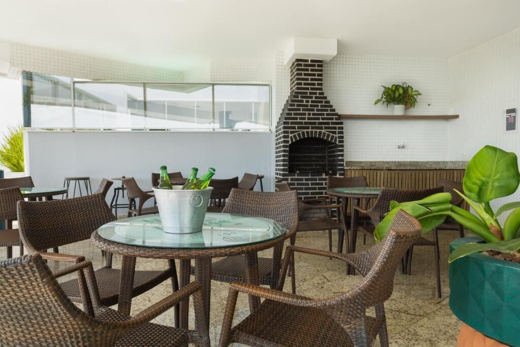 An outdoor seating area with wicker chairs and a glass table, a brick fireplace, and a potted plant.