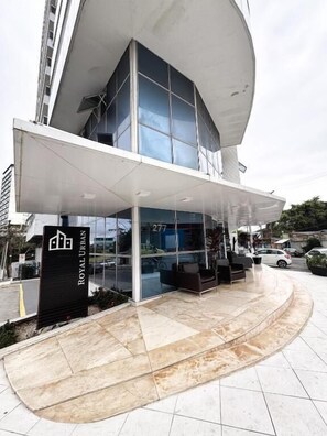 Un edificio moderno con fachada de vidrio, un acceso cubierto y un letrero que dice "ROYAL URBAN".