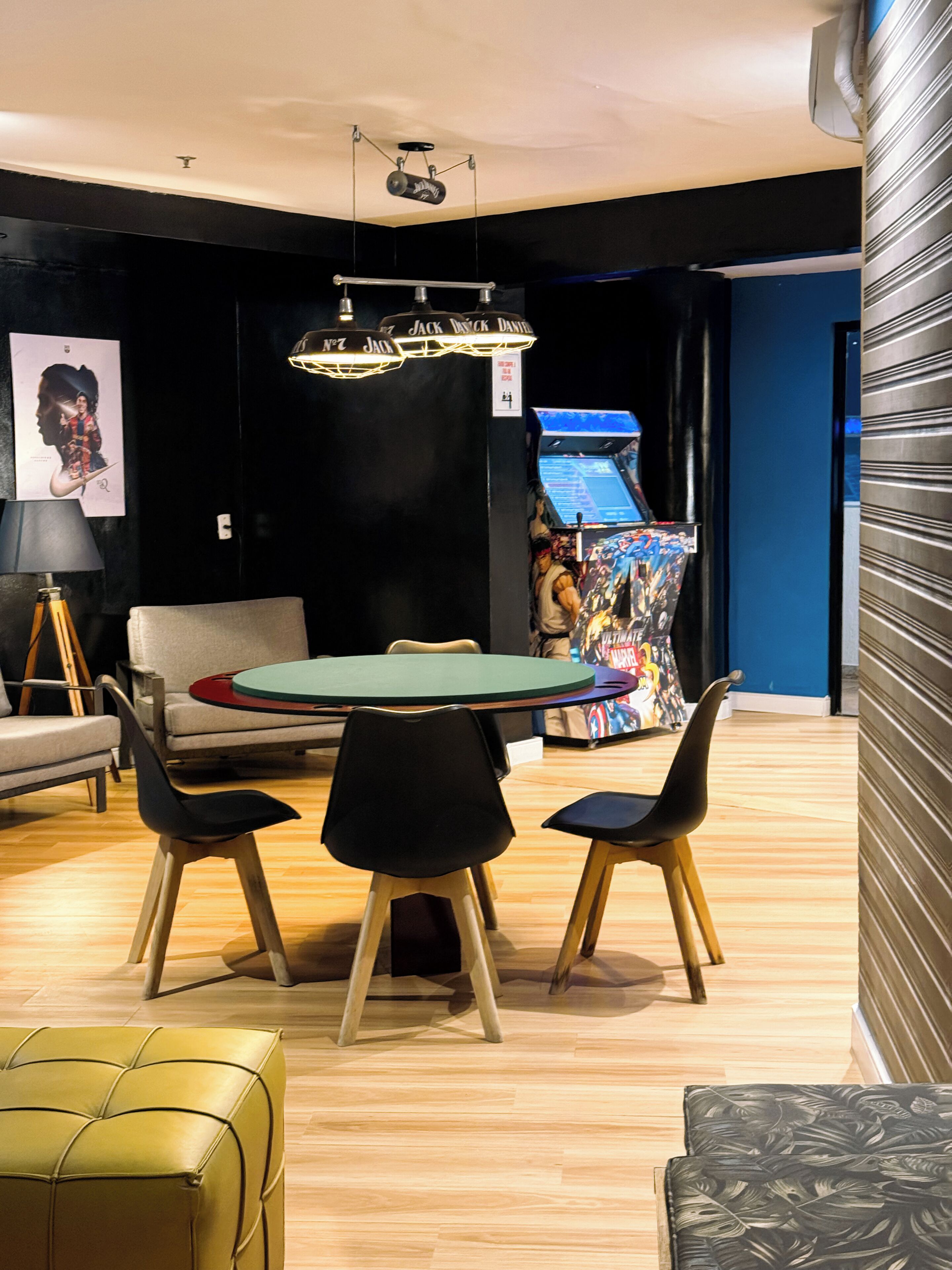 A modern room with a round table, four chairs, a sofa, a lamp, and a gaming machine.