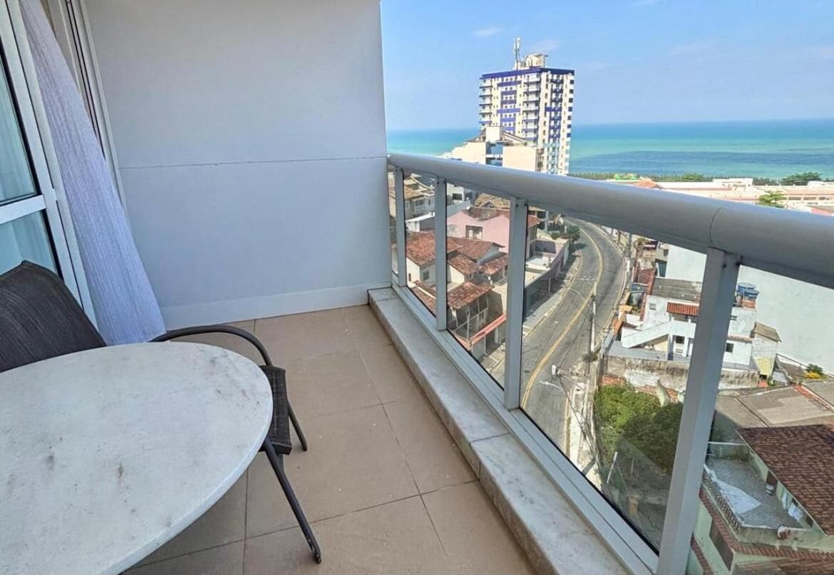 Un balcón con vistas a una ciudad costera, incluyendo un edificio alto y una carretera.