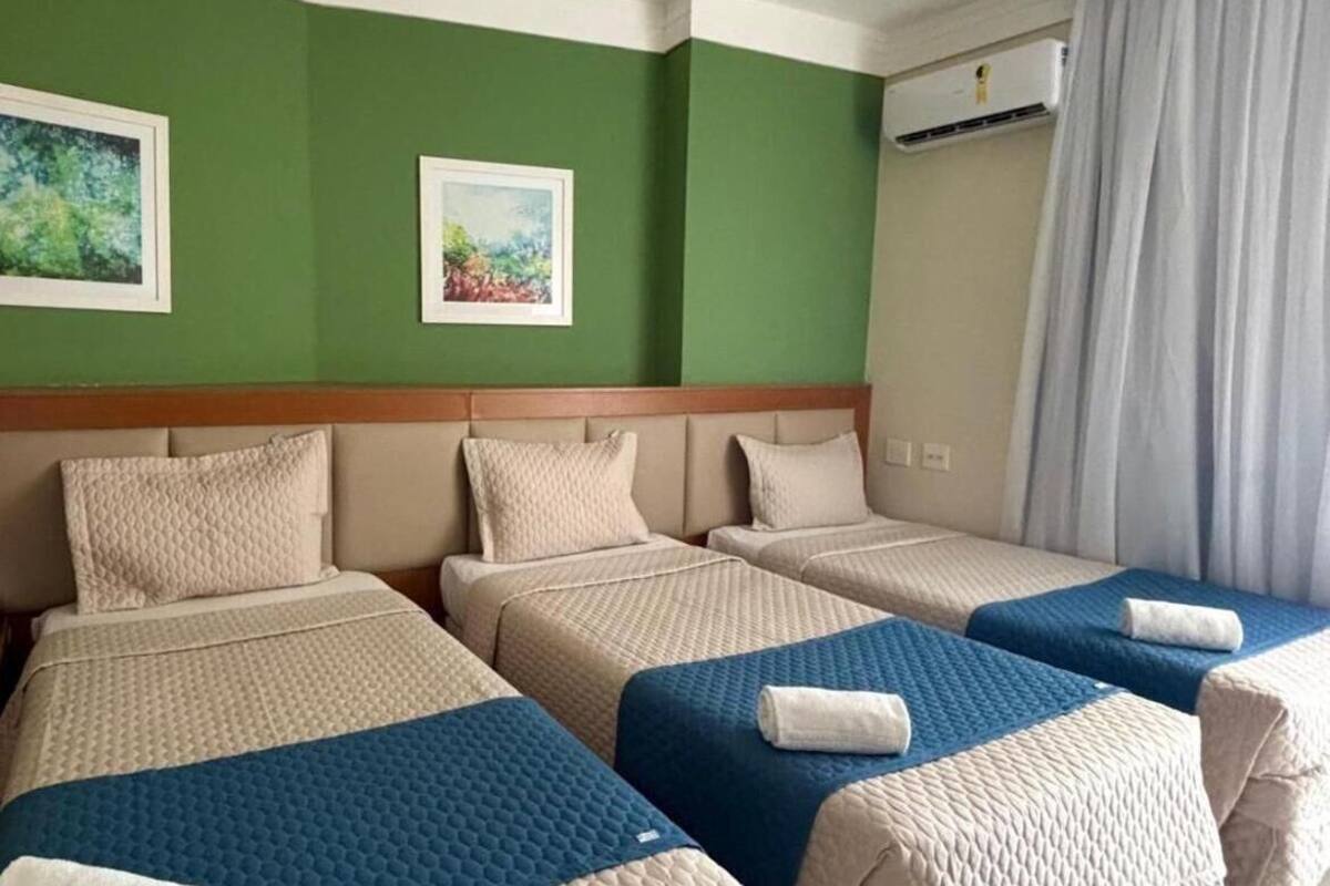 A hotel room with four beds arranged in a row, green walls, and two framed pictures.