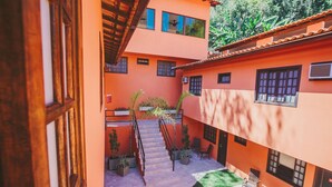 Un patio con una escalera que lleva a un nivel superior, rodeado de paredes anaranjadas y plantas en macetas.