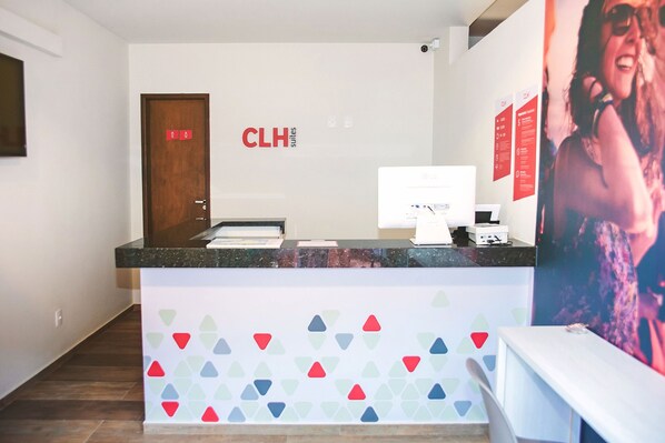 A hotel reception desk with a modern design, a computer monitor, and a wall-mounted sign reading "CLH suites". - CLH Suítes Ilha Grande - Hostel (Angra dos Reis)