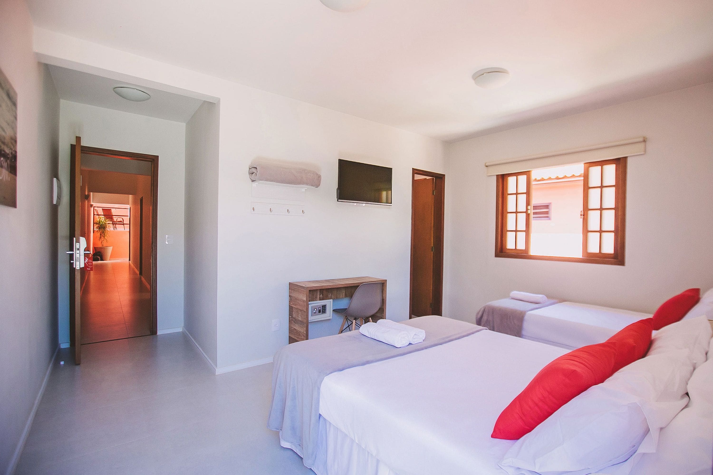 A hotel room with two beds, a desk, a chair, a TV, and a window with blinds.