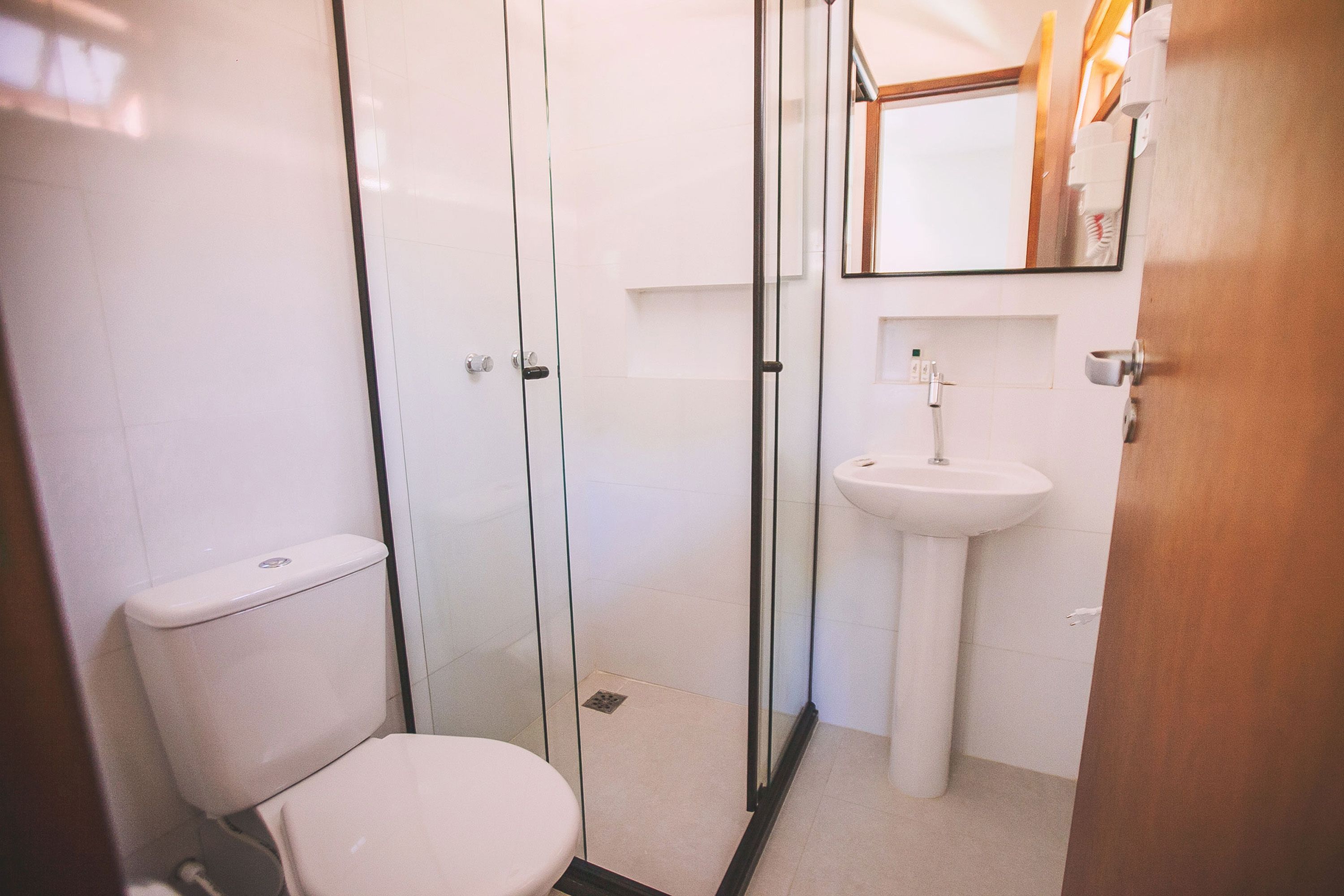 Une salle de bain moderne avec une douche à parois de verre, des toilettes blanches et un lavabo sur colonne.