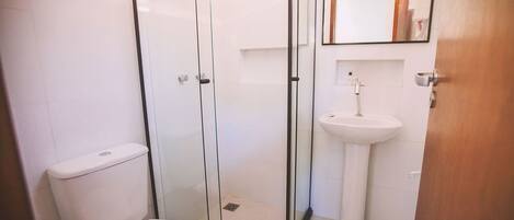 Un baño moderno con ducha envuelta en vidrio, inodoro blanco y lavamanos sobre pedestal.