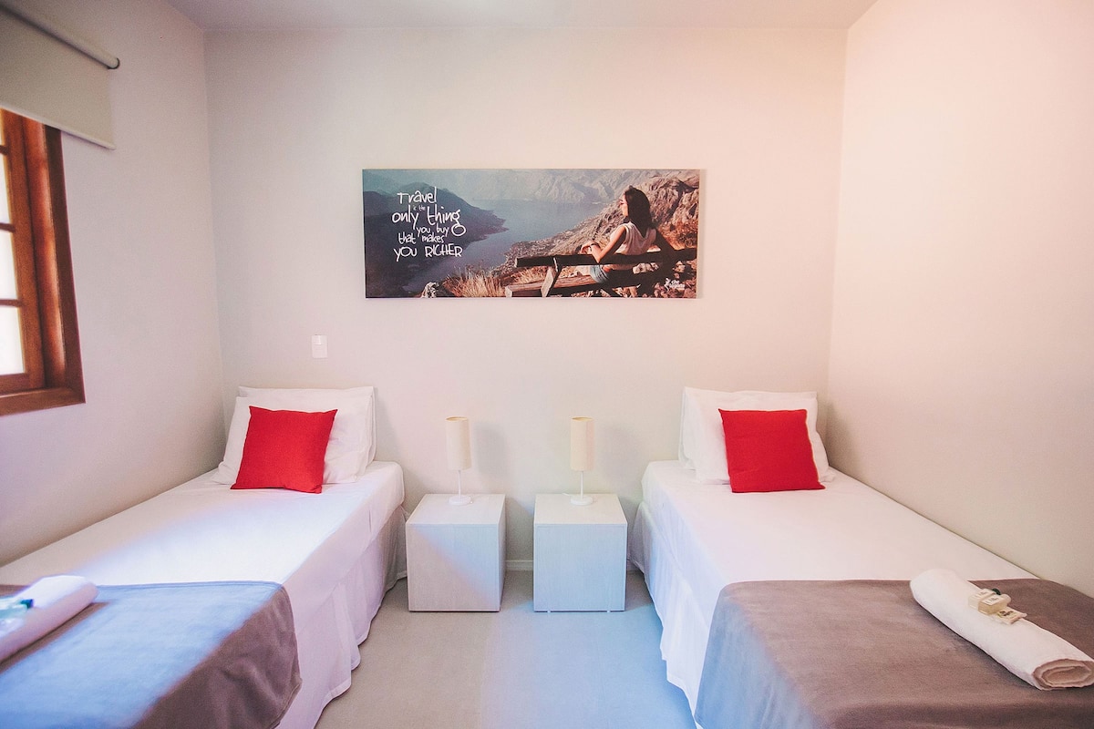 A hotel room with two single beds, a small table, a nightstand, and a wall-mounted picture.