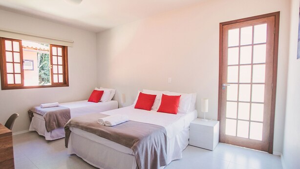 Habitación de hotel con dos camas, una puerta de madera, una ventana con persianas y una mesita de noche pequeña.