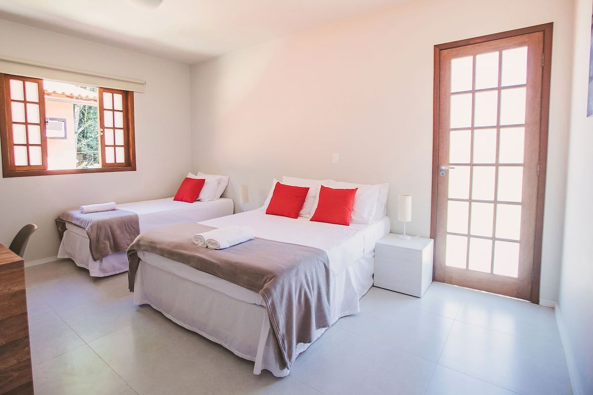 A hotel room with two beds, a wooden door, a window with blinds, and a small bedside table.