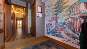 A hallway with wooden flooring, a stone-tiled landing, and a colorful mural depicting Kyoto architecture. - Shiki Homes SHINJIN (Kyoto)
