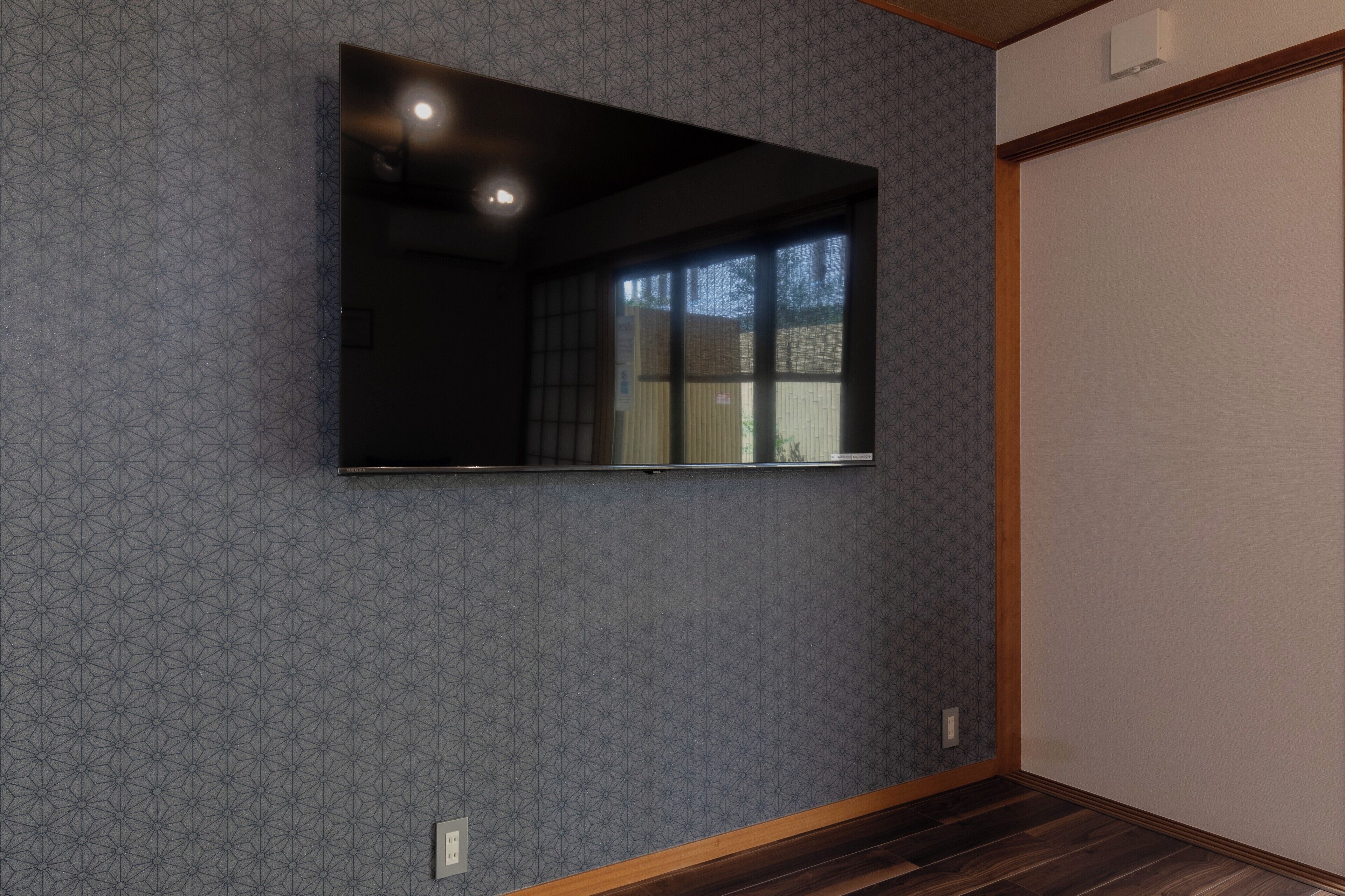 Quarto com papel de parede estampado, televisão de tela plana fixada na parede e piso de madeira.
