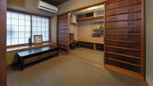 A traditional Japanese room with tatami flooring, a sliding door, a wooden bench, a desk, and a painting on the wall. - Shiki Homes SHINJIN (Kyoto)