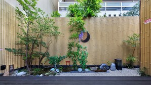 A bamboo fence with various plants and rocks, a small red stool, and a black lantern. - Shiki Homes SHINJIN (Kyoto)
