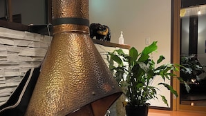 A modern fireplace with a textured metallic finish, a fire burning inside, and a potted plant nearby. - Bears Den Mountain Lodge (Hakuba)