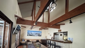 A spacious dining area with a long wooden table and benches, a kitchen area with a stone countertop, and a high ceiling with exposed wooden beams. - Bears Den Mountain Lodge (Hakuba)