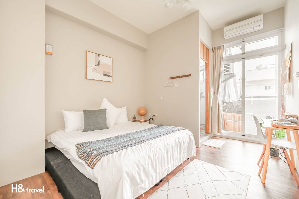 Une chambre à coucher avec un lit, une table de chevet, une lampe et une vue sur le balcon extérieur.