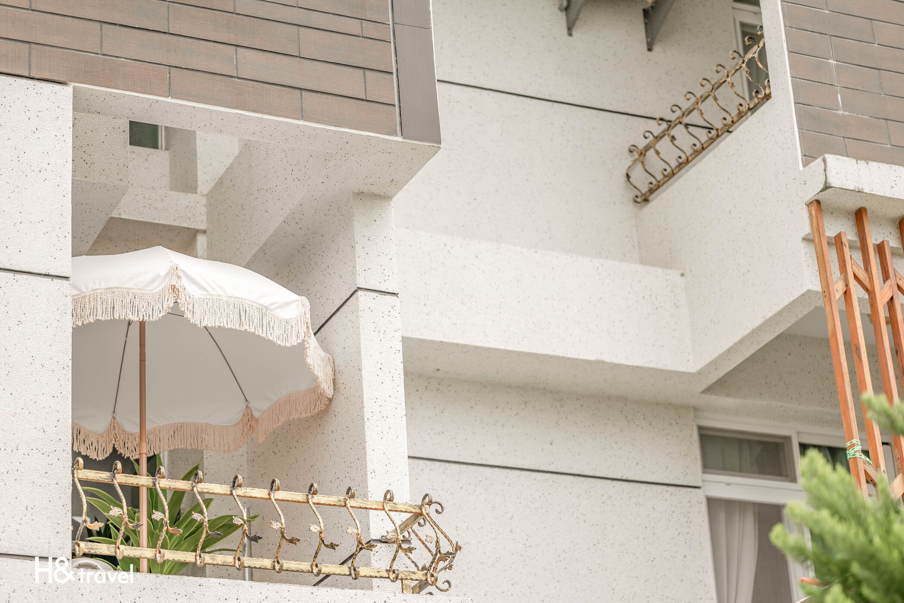 A modern building with a balcony featuring a white umbrella and a metal railing.