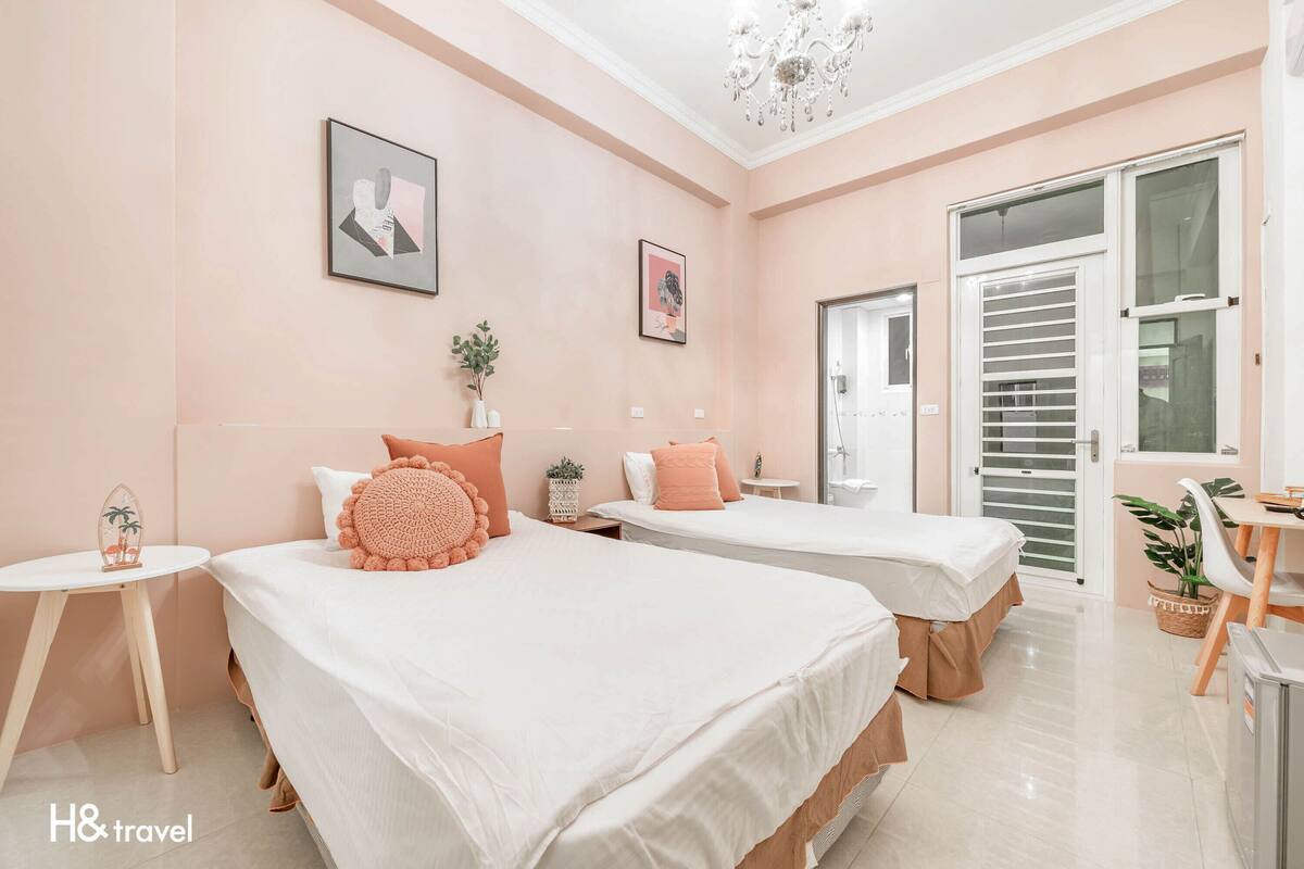 Une chambre d’hôtel avec deux lits, une petite table, une chaise, une plante en pot et une porte avec une fenêtre.