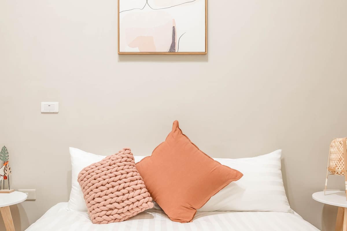 Une chambre à coucher avec un lit, deux oreillers, une petite table avec une plante et un tableau accroché au mur.