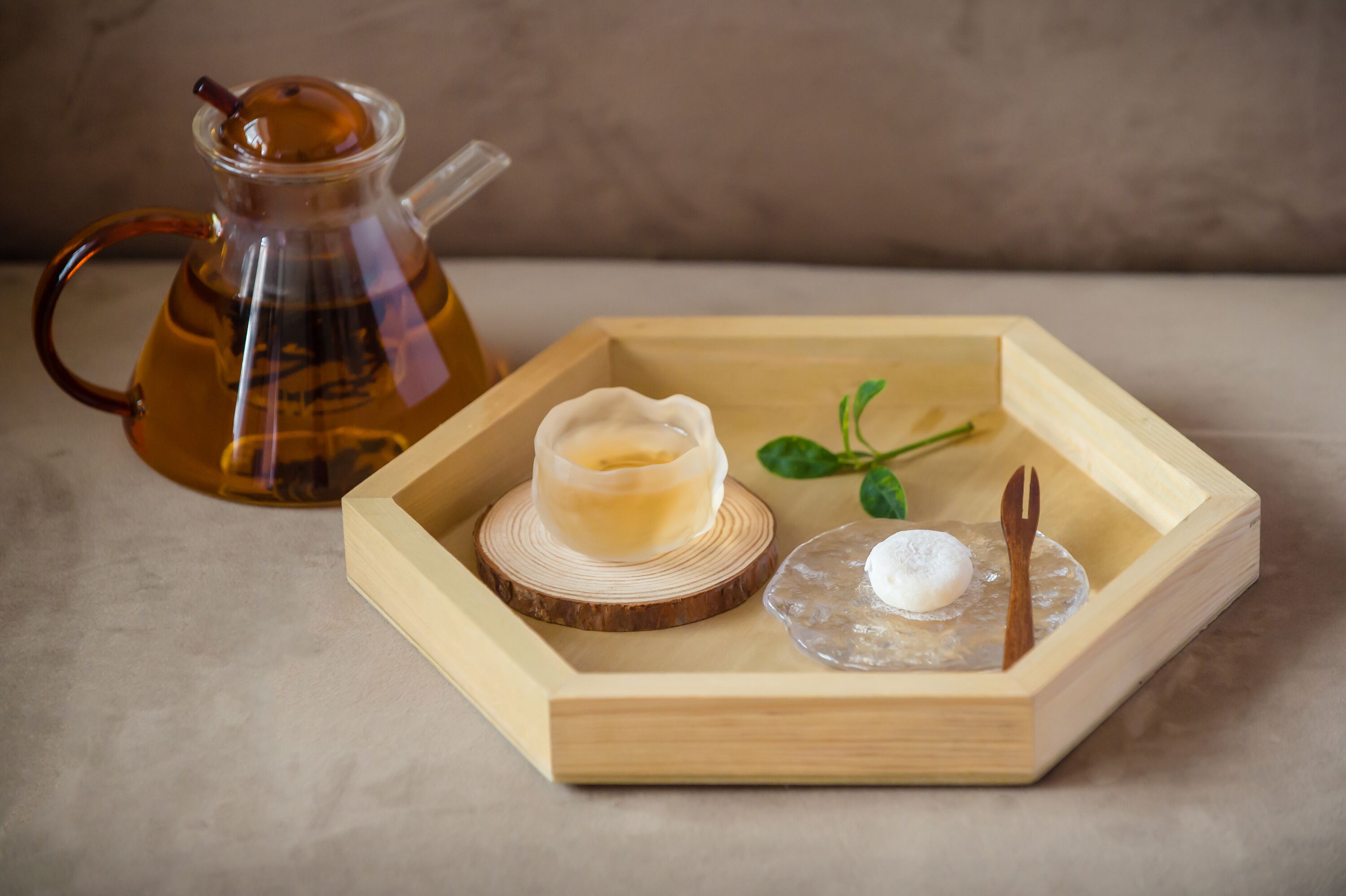 A wooden tray with a glass teapot, a small jar, and a spoon.