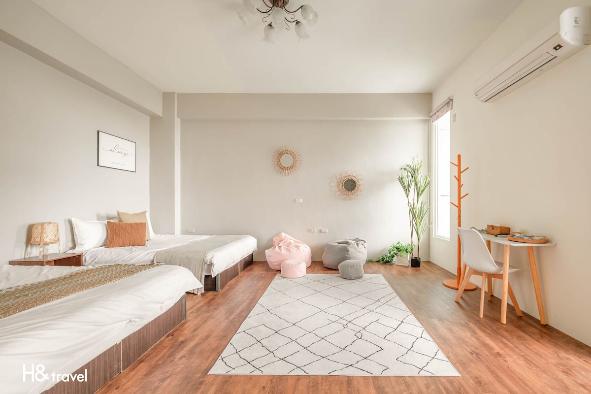Une chambre d’hôtel moderne avec deux lits, un bureau et une chaise. Les murs sont décorés et il y a une plante en pot.