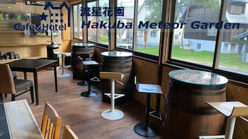 A cafe and hotel interior with wooden furniture, large windows, and a view of the outside.