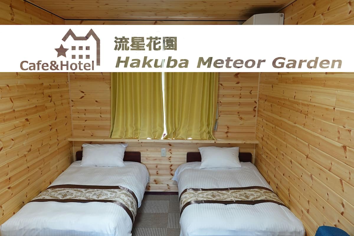 Ein Zimmer mit zwei Betten, Holzwänden, einem Fenster mit Vorhängen und einem Schild für Cafe&Hotel Hakuba Meteor Garden.
