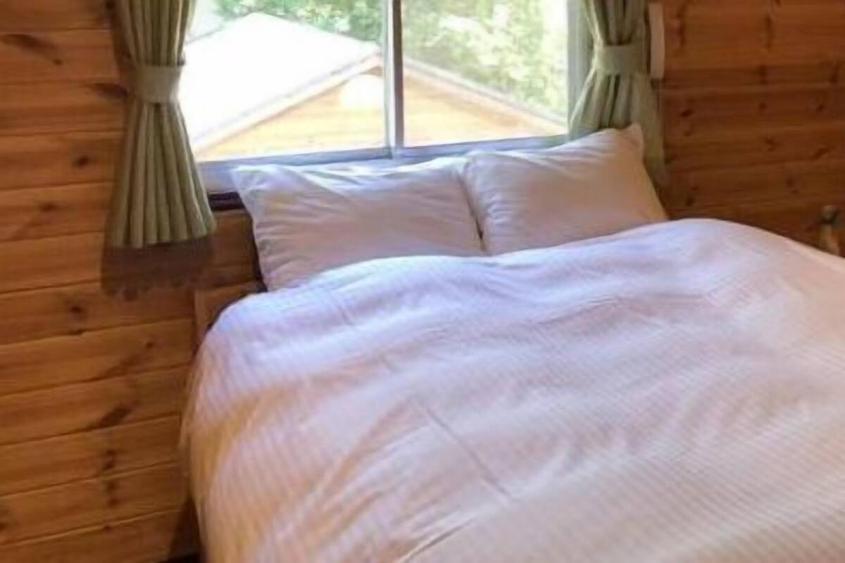 Ein Zimmer in einer Holzhütte mit einem Bett, Vorhängen und einem Fenster.