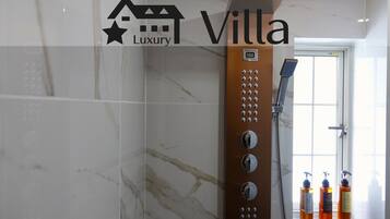 A bathroom with a shower, marble tiles, and three bottles of shampoo on a shelf.