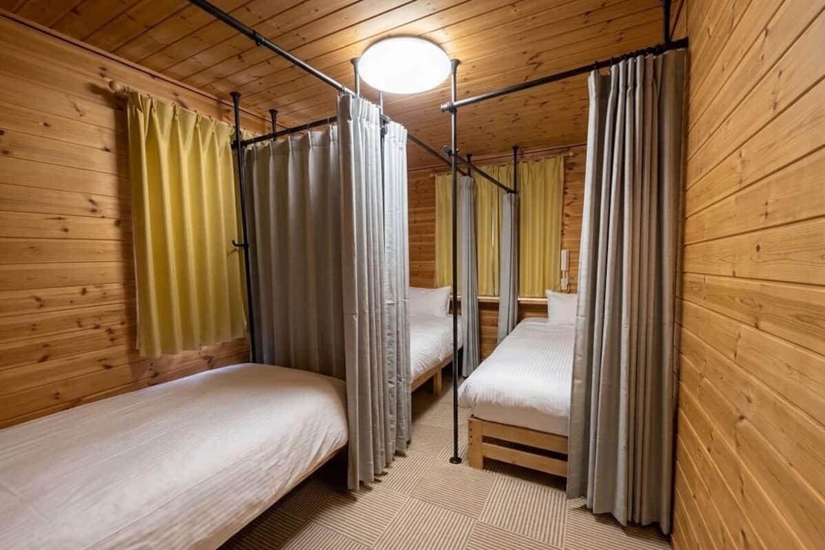 Ein blockhaushaltiger Raum mit Holzwänden, zwei Einzelbetten, einer Deckenleuchte und einem Fenster mit Vorhängen.
