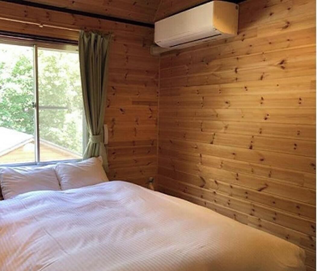 A wooden cabin room with a bed, a window with curtains, and an air conditioning unit.