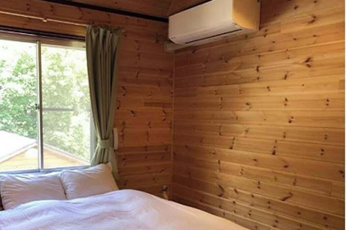 Ein Zimmer in einer Holzhütte mit einem Bett, einem Fenster mit Vorhängen und einer Klimaanlage.
