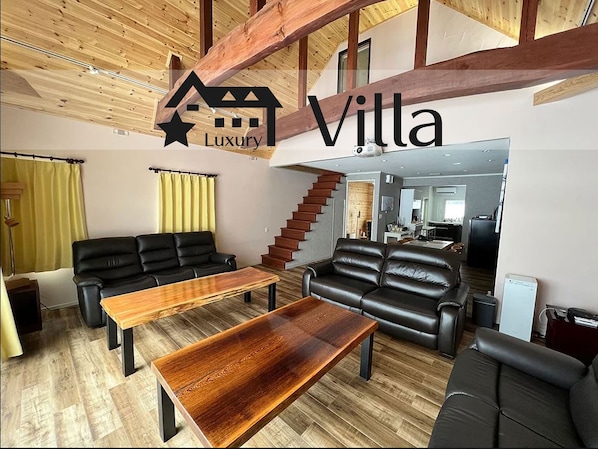A spacious living area with a wooden ceiling, black leather sofas, and a wooden coffee table. - Meteor Garden (Hakuba)