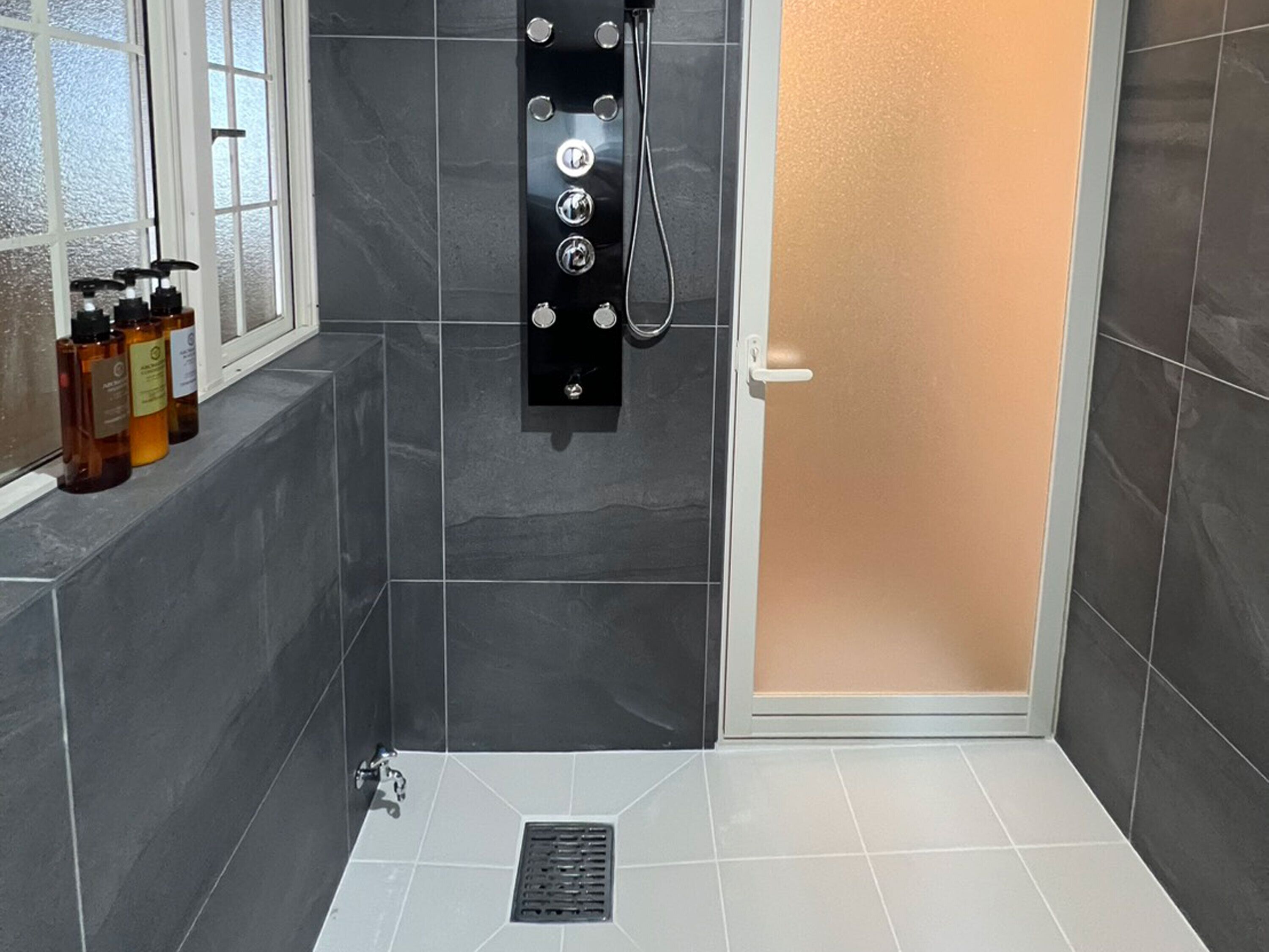 A modern bathroom with a shower, a window, and a shelf with toiletries.