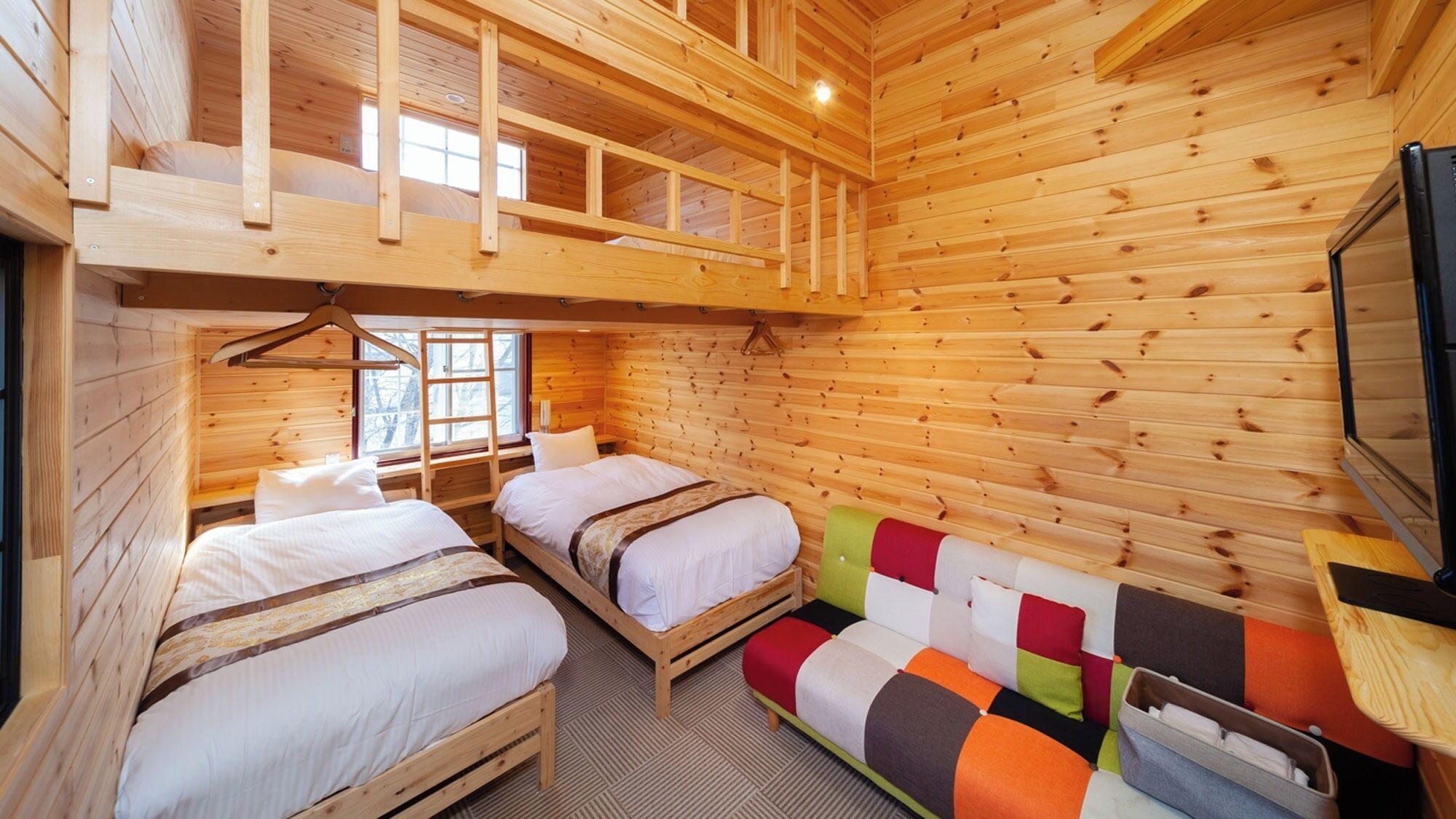 A cabin with two wooden beds, a loft bed, a colorful sofa, and a television.