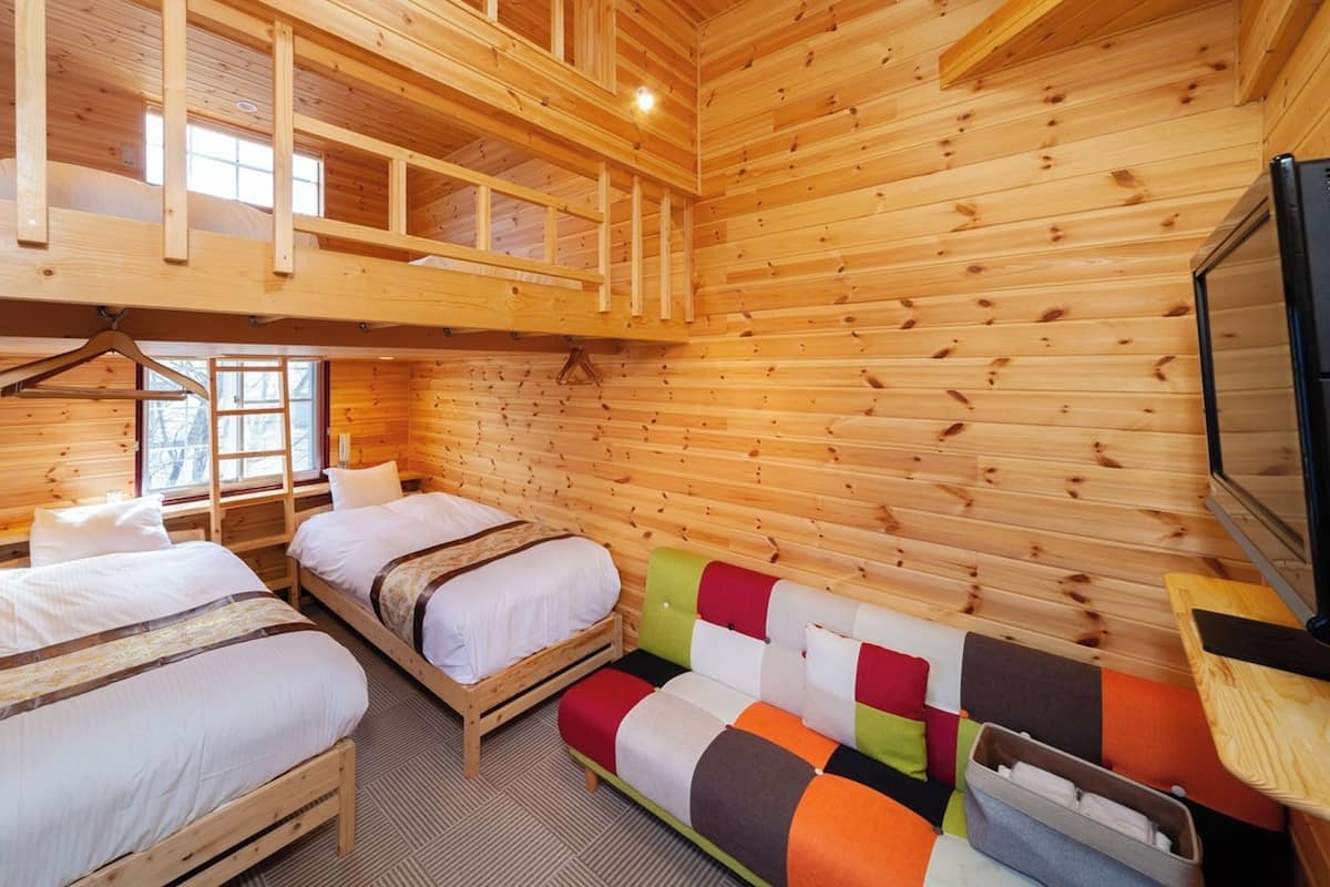 Eine Hütte mit zwei Holzbetten, einem Schlafbett im Hochbett und einem bunten Sofa sowie einem Fernseher.