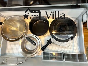 A kitchen with three black pans, a metal strainer, and a white appliance with a grid pattern.