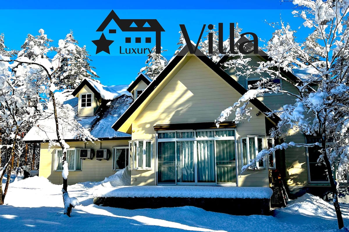 Eine villa mit Schnee bedeckt, mit einem großen Fenster, einer Tür und einer sichtbaren Treppe, die zum Eingang führt.