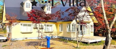 A yellow villa with a grey roof, surrounded by trees with red leaves.