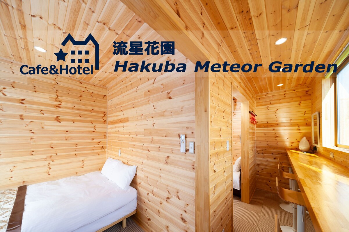 A wooden cabin interior with a bed, a small table, and a window.