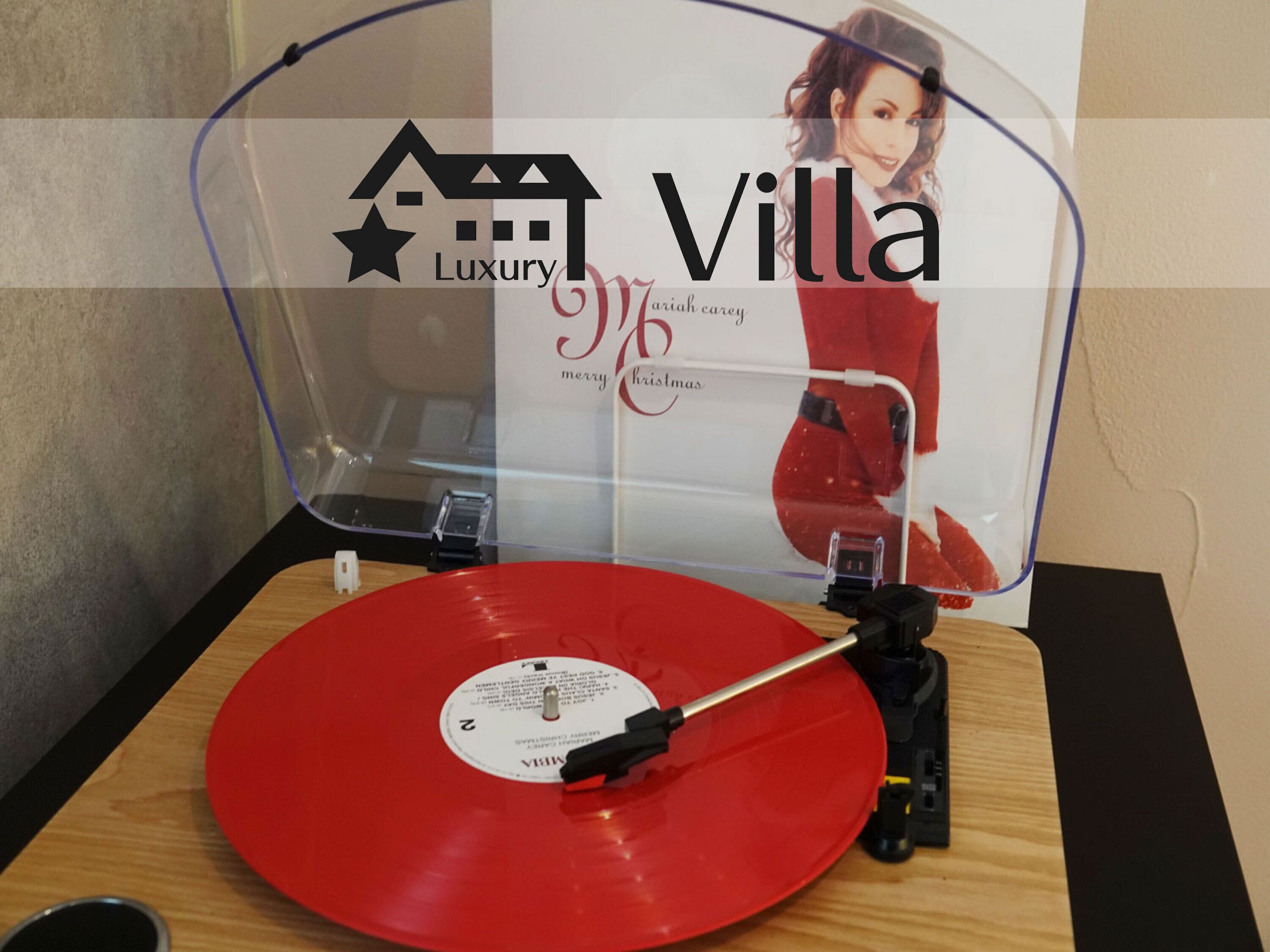 Tocadiscos con un disco de vinilo rojo, una cubierta protectora transparente y un letrero con los textos 'Villa Luxury' y 'feliz navidad' al fondo.