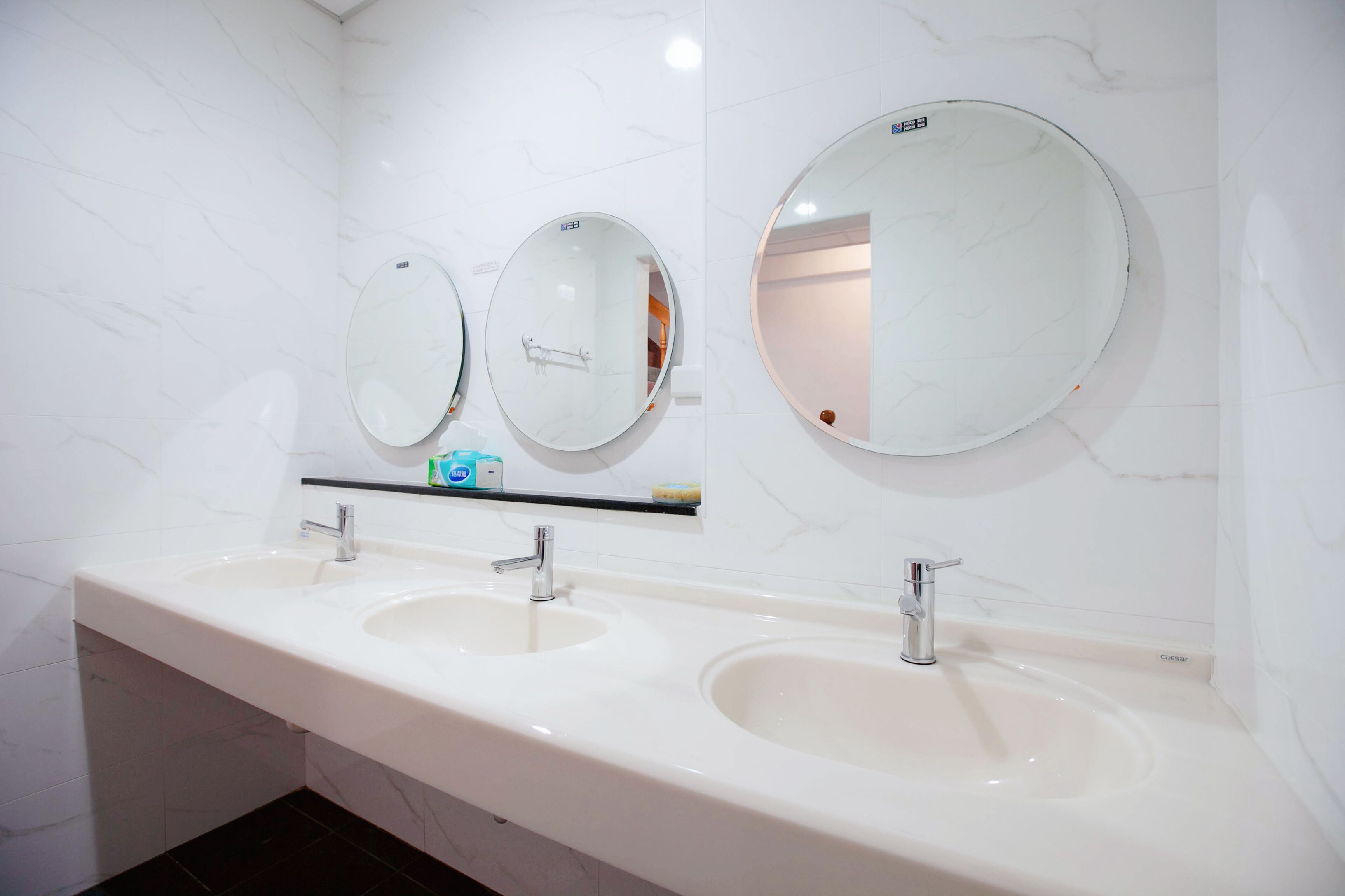 A bathroom with two sinks, a mirror, and a soap dispenser on a shelf.