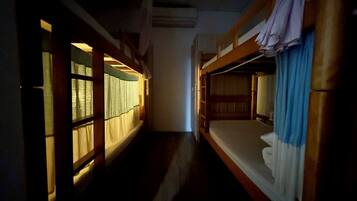 A narrow corridor with bunk beds on either side, wooden walls, and a window with curtains.
