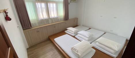 Habitación de hotel con tres camas individuales, piso de madera, ventana con cortinas, un radiador y una puerta con picaporte.