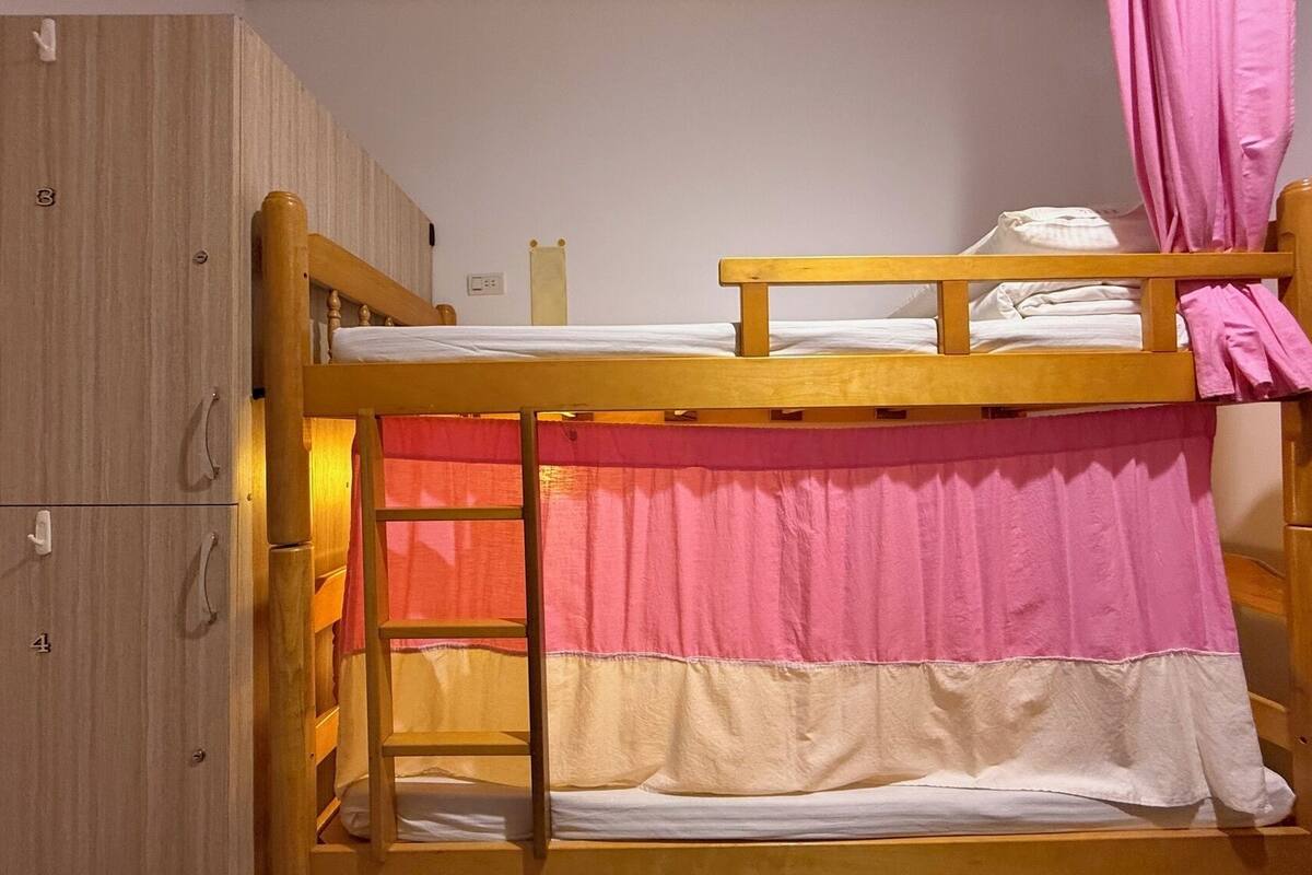 A bunk bed with a wooden ladder, pink curtains, and a wooden wardrobe.